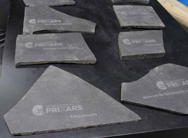 Mehrere Schieferplatten mit dem Logo „Prix Ars Electronica“ und verschiedenen Aufschriften liegen auf einem Tisch.