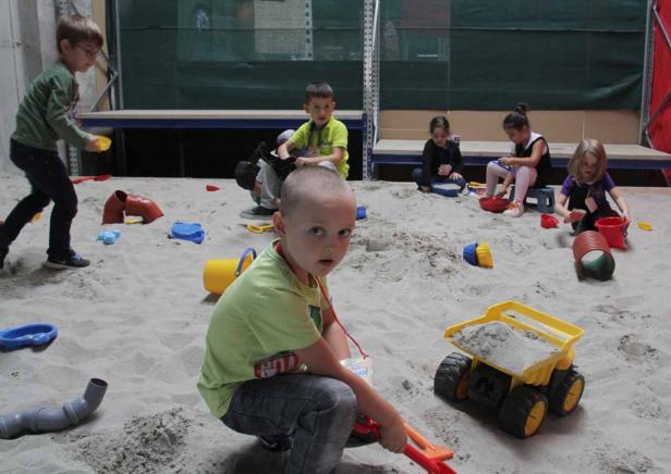Mehrere Kinder spielen in einem Sandkasten mit Förmchen und einem Spielzeug-LKW.