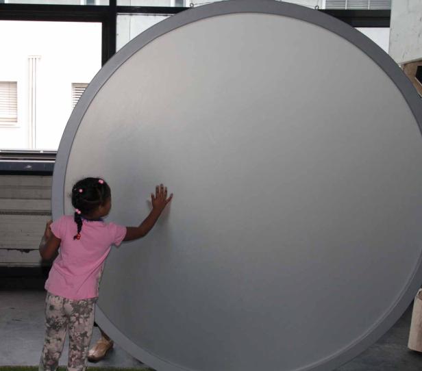 Ein kleines Mädchen berührt eine große, runde, graue Oberfläche.