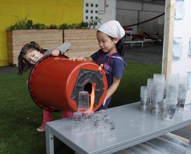 Zwei Mädchen spielen mit einem großen, orangefarbenen Behälter und Plastikbechern.