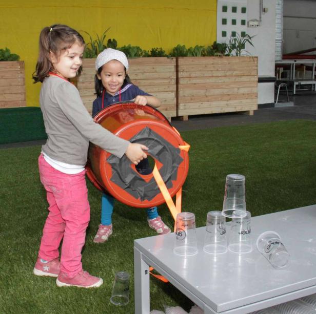 Zwei Mädchen spielen mit einem Fass und versuchen, Plastikbecher umzuwerfen.