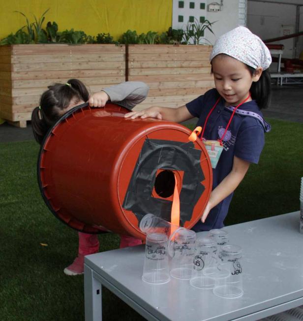 Zwei Mädchen spielen mit einem umgebauten Eimer und befüllen Plastikbecher.