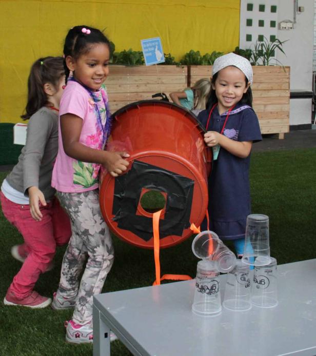 Drei Mädchen spielen ein Spiel mit einem umgedrehten Eimer und Plastikbechern.