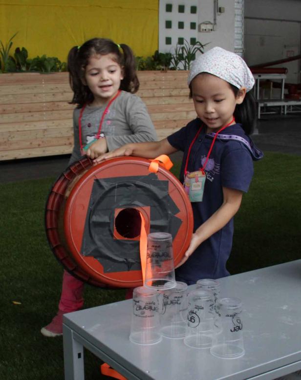 Zwei Mädchen spielen mit einem selbstgemachten Spielzeug aus Eimer und Plastikbechern.