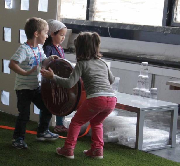 Drei Kinder hantieren mit einem großen Schokoladenosterei und Plastikbechern.