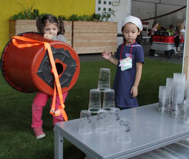 Zwei Mädchen spielen mit einem umgebauten Fass und Plastikbechern.