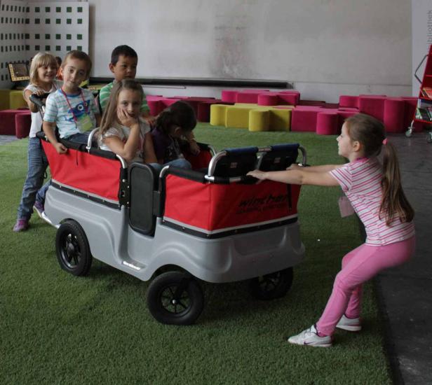 Eine Gruppe Kinder sitzt in einem Wagen, der von einem Mädchen gezogen wird.