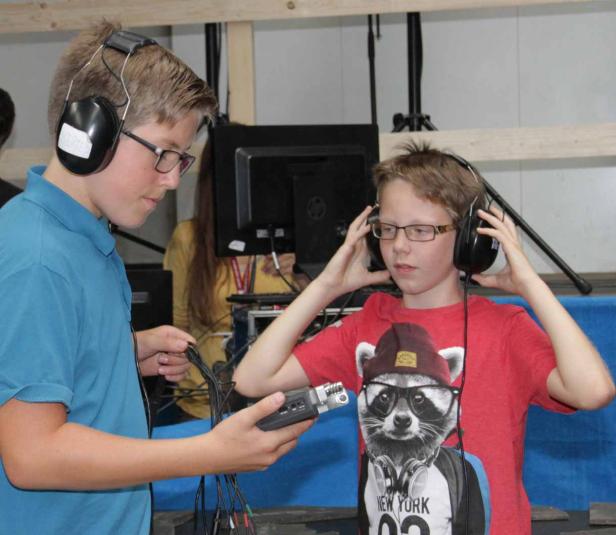 Zwei Jungen mit Kopfhörern hantieren mit einem Aufnahmegerät.