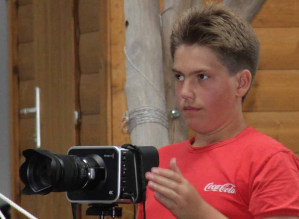 Ein junger Mann mit einem roten T-Shirt steht vor einer 4K-Kamera.