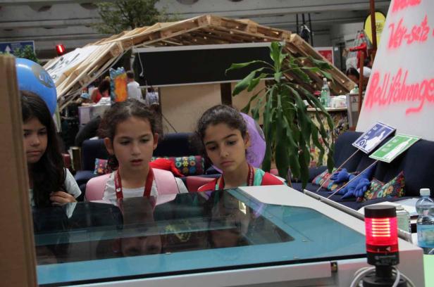 Drei Mädchen stehen vor einem Gerät mit einer Glasplatte und schauen hinein.