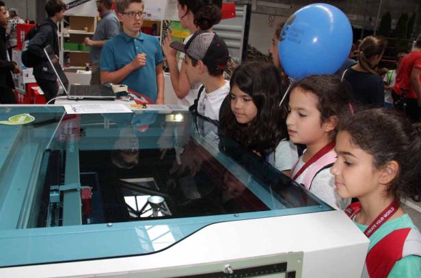Eine Gruppe Kinder beobachtet eine Laserschneidemaschine bei der Arbeit.