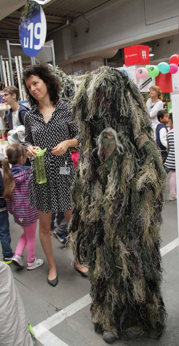 Eine Frau steht neben einer Person im Ghillie-Anzug.