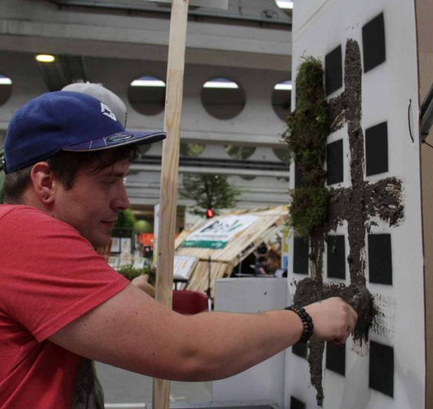 Ein Mann bepflanzt eine Wand mit Moos, um ein Gebäude darzustellen.