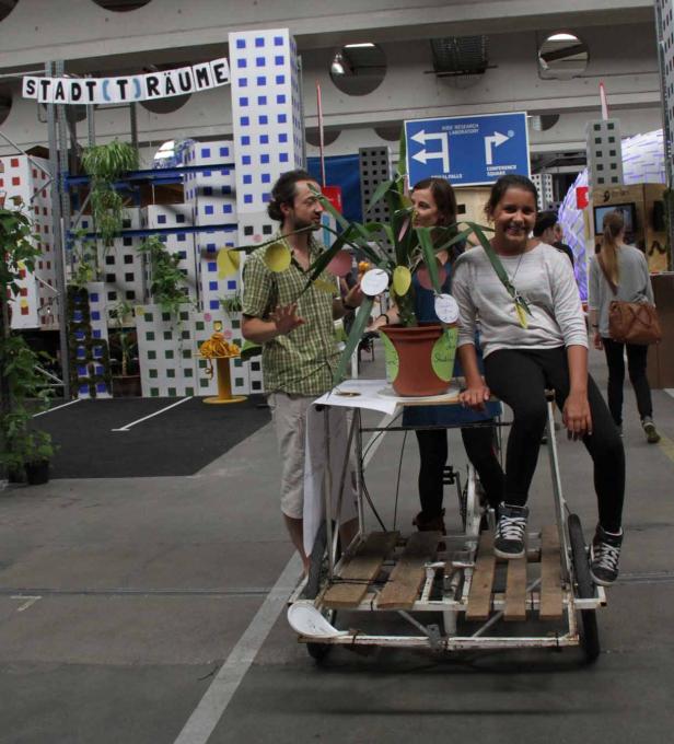 Drei Personen stehen an einem dekorierten Fahrrad vor dem Hintergrund „Stad(t)räume“.