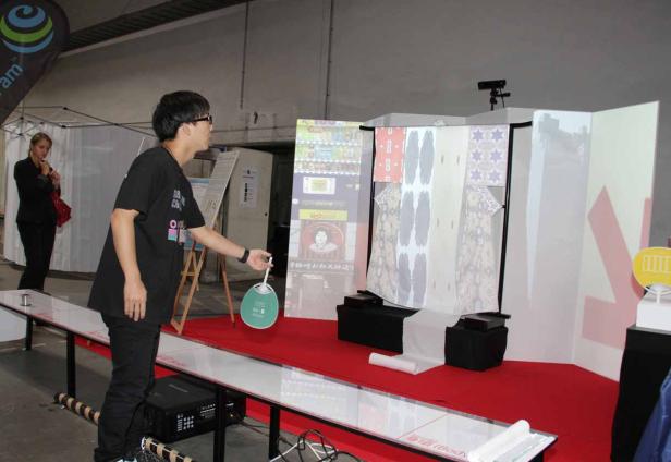 Ein Mann steht vor einer Installation mit projizierten Bildern und hält einen Fächer.