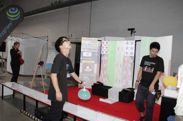 Ein Mann mit Brille spielt mit einem Fächer vor einem japanisch inspirierten Stand.