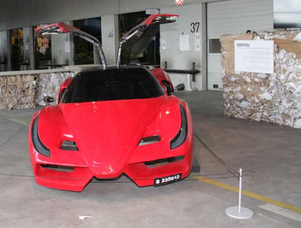 Ein roter Sportwagen mit geöffneten Flügeltüren steht in einer Lagerhalle.