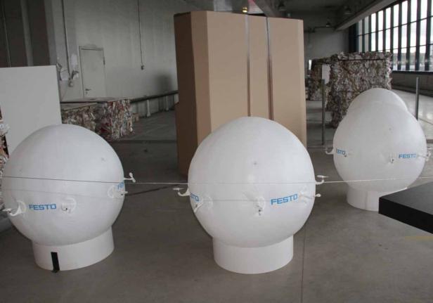 Drei weiße Festo-Kugeln stehen in einem Raum mit Kartons und anderem Material.