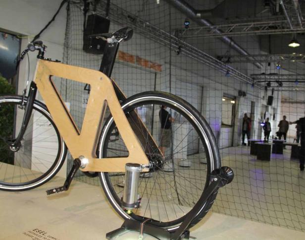 Ein Fahrrad mit einem Rahmen aus hellem Holz steht auf einem Präsentationsständer.