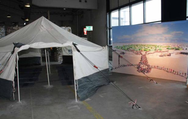 Ein Zelt steht vor einem großen Bild mit einer Menschenkette in einer Wüstenlandschaft.