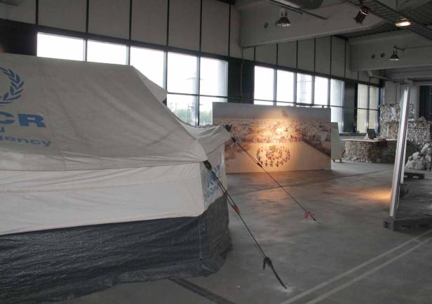Ein UNHCR-Zelt steht in einem Ausstellungsraum vor einem großen Foto.