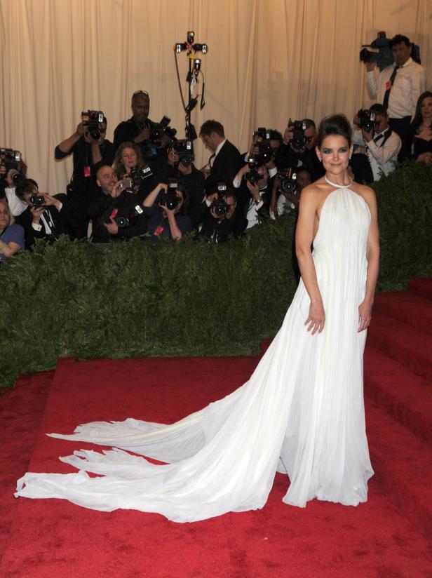 Katie Holmes in einem weißen Kleid auf einem roten Teppich, umgeben von Fotografen.