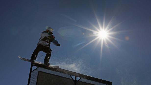 Ein Snowboarder springt bei strahlendem Sonnenschein über eine Rampe.