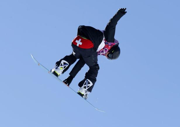 Ein Snowboarder mit Schweizer Flagge auf der Hose springt in der Luft.