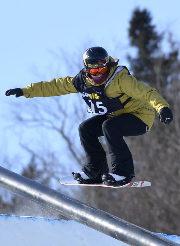 Eine Snowboarderin springt über eine Metallstange.