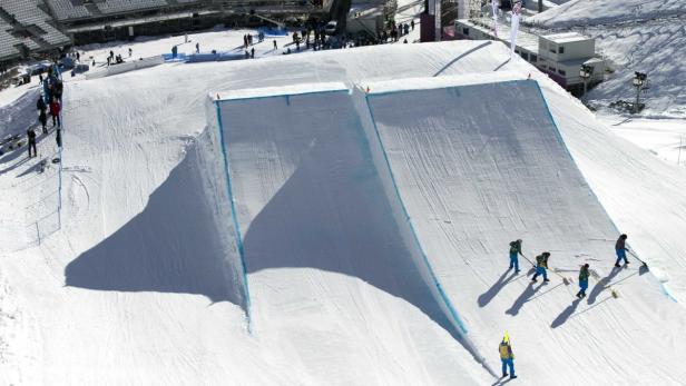 Arbeiter präparieren eine Halfpipe für ein Snowboard-Event.