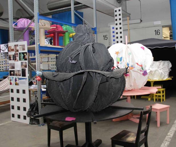 Eine große, schwarze Skulptur steht auf einem runden Tisch in einem Lagerraum.