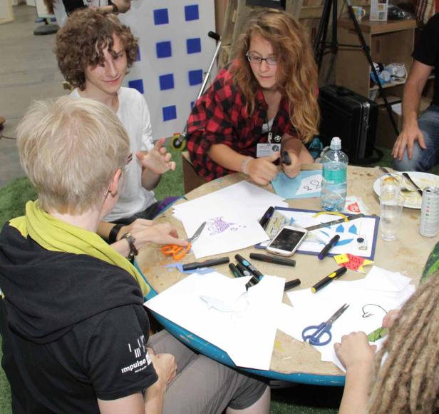 Eine Gruppe von Menschen sitzt an einem Tisch und bastelt mit Papier, Scheren und Stiften.