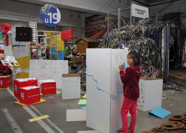 Ein junges Mädchen zeichnet ein Herz auf eine weiße Tafel in einer Ausstellung.