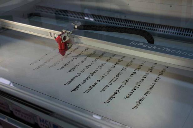 Ein Lasergerät graviert einen Text mit dem Schriftzug „InPack-Techno“ in ein Material.