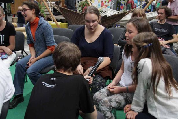 Eine Frau wird von einer anderen Person mit einem Mikrofon interviewt, während andere Personen um sie herum sitzen.