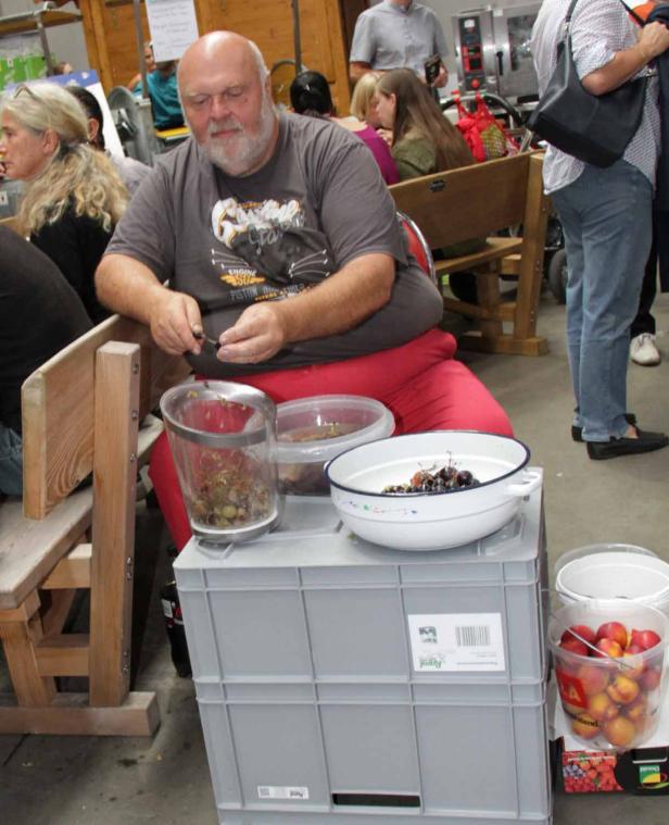 Ein Mann entsteint Kirschen an einem Tisch mit mehreren Schüsseln voll Früchten.