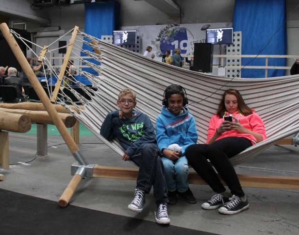 Drei Kinder entspannen in einer großen Hängematte in einer Halle.
