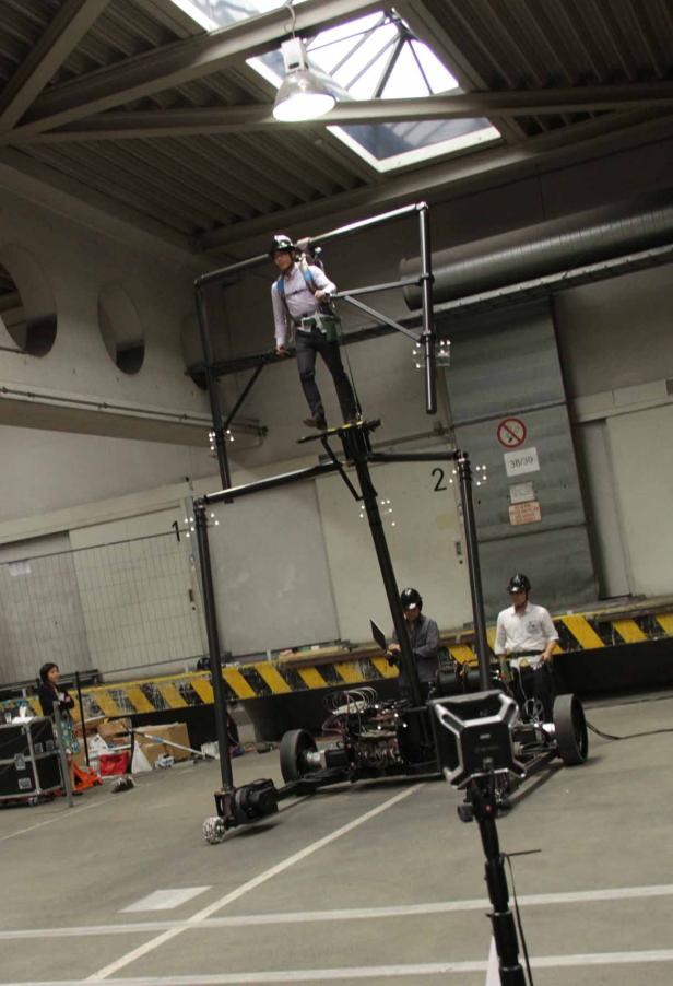 Eine Person steht auf einer beweglichen Plattform mit Sicherheitsausrüstung in einer Lagerhalle.