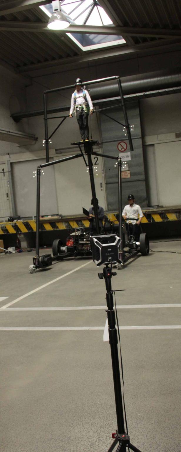 Ein Mann steht gesichert auf einer hohen, fahrbaren Kamerabühne in einer Lagerhalle.