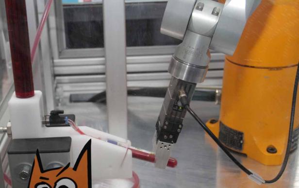 Ein Roboterarm hält ein Reagenzglas mit einer roten Flüssigkeit.