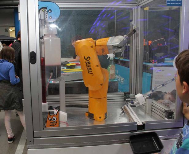 Ein gelber Roboterarm von Stäubli steht in einem Glaskasten.