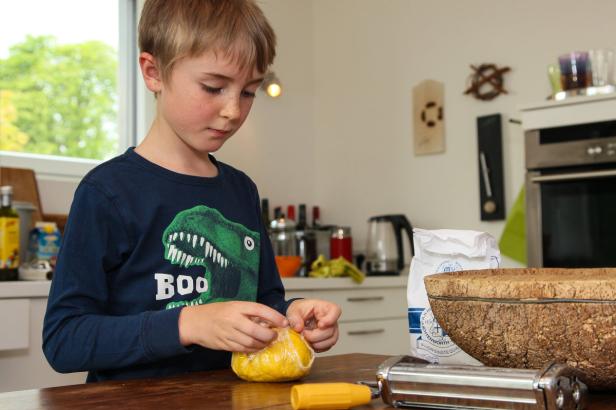 Ein Junge mit einem Dinosaurier-T-Shirt verpackt Teig in Frischhaltefolie.