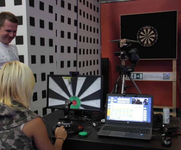 Eine Frau spielt ein Dartspiel mit einem Joystick vor einem Computerbildschirm.