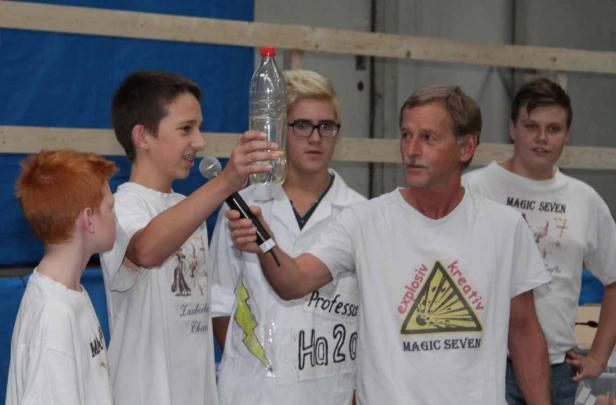 Eine Gruppe von Kindern und ein Mann präsentieren ein Experiment mit einer Wasserflasche.