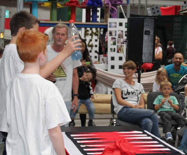 Ein rothaariger Junge führt vor Publikum einen Zaubertrick mit einer Wasserflasche vor.