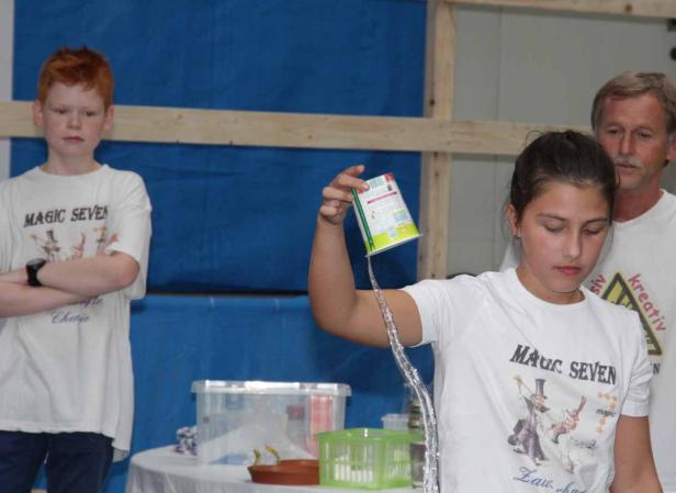 Ein Mädchen gießt Wasser aus einem Becher, während ein Junge und ein Mann zusehen.