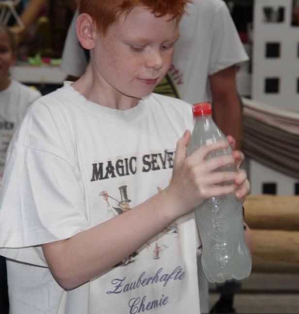 Ein rothaariger Junge hält eine Plastikflasche mit einer klaren Flüssigkeit in den Händen.