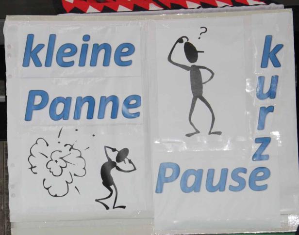 Ein Plakat mit den Wörtern „kleine Panne“, „kurz“ und „Pause“ sowie Strichmännchen-Zeichnungen.