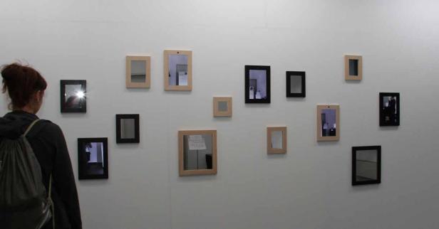 Eine Frau betrachtet eine Wand mit kleinen Spiegeln in verschiedenen Rahmen.