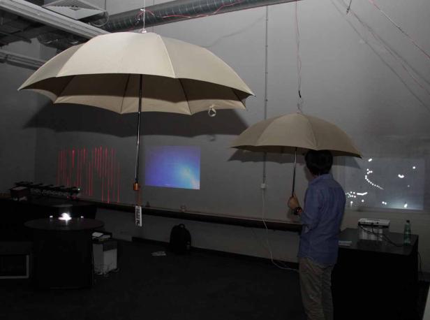 Ein Mann steht unter einem Regenschirm in einem Raum mit Projektionen an der Wand.